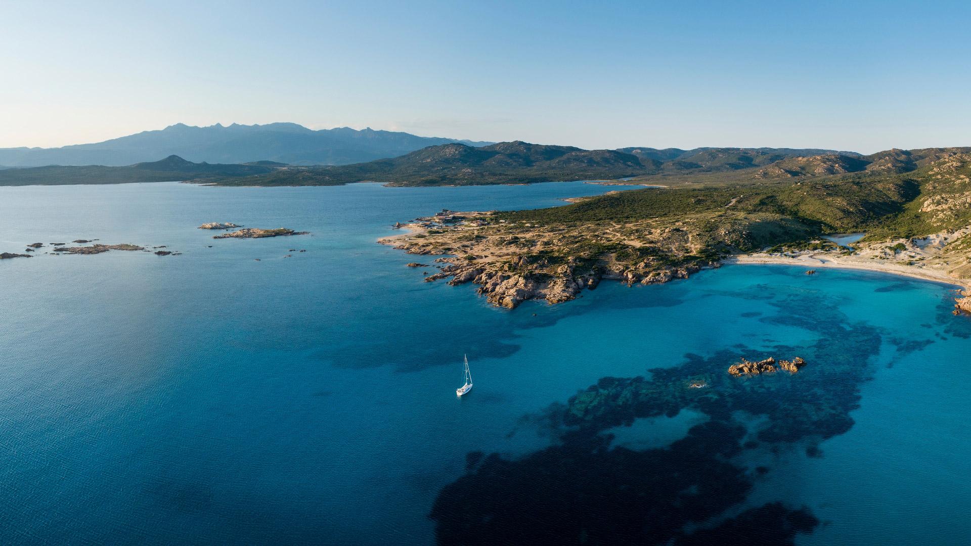 Vista aerea di una costa rocciosa con mare cristallino e barca a vela.