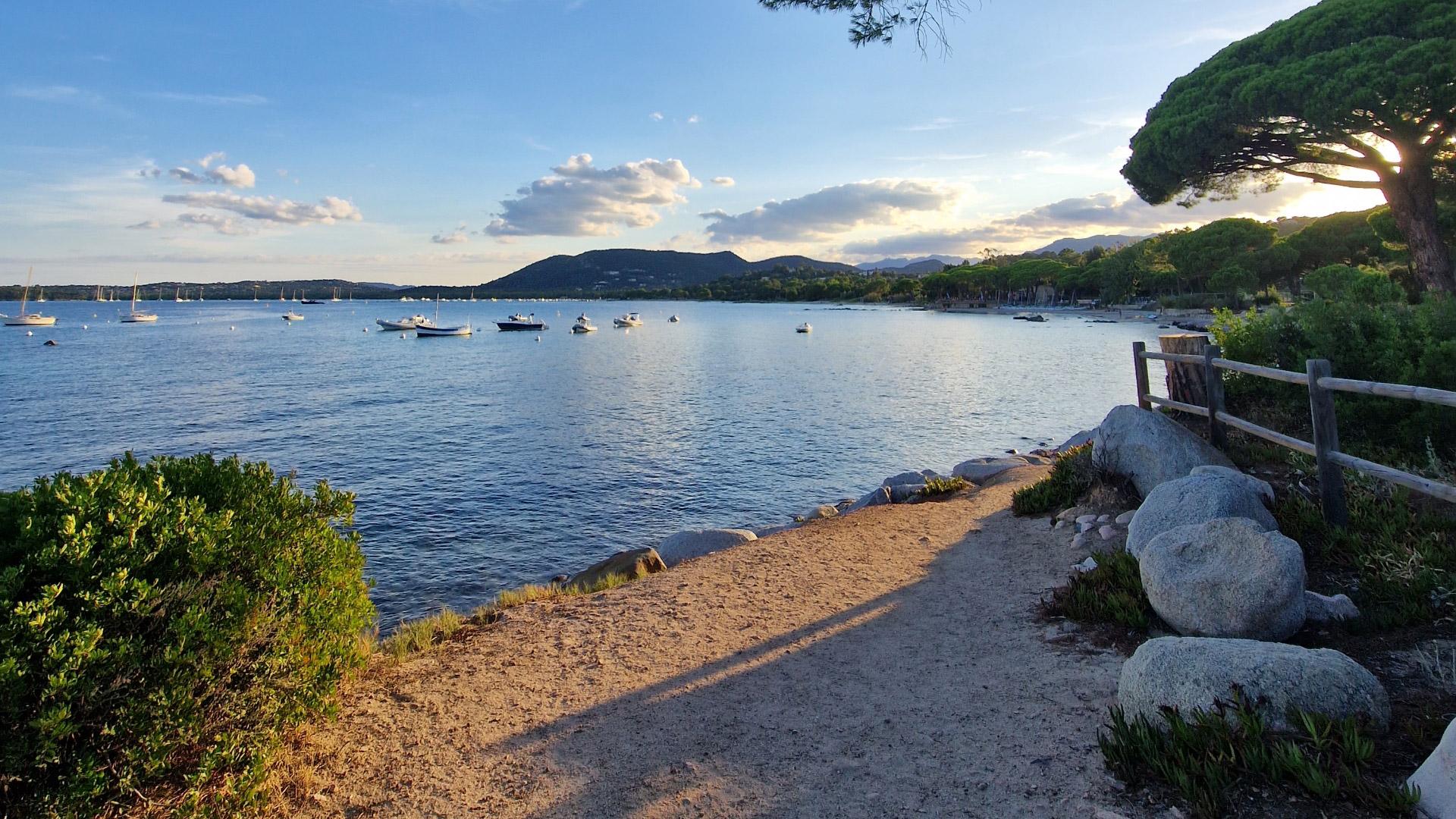 Sentiero costiero con vista sul mare e barche, al tramonto.