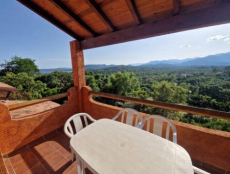 Terrazza con vista panoramica su foresta e montagne, tavolo e sedie bianche.