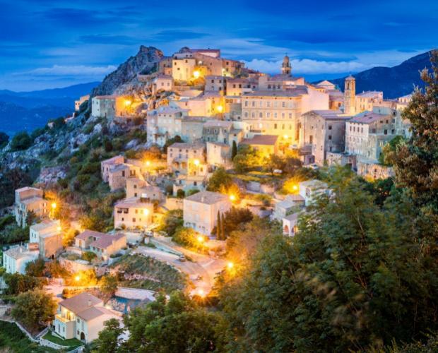 Un pittoresco villaggio montano illuminato, incastonato tra le colline al tramonto.