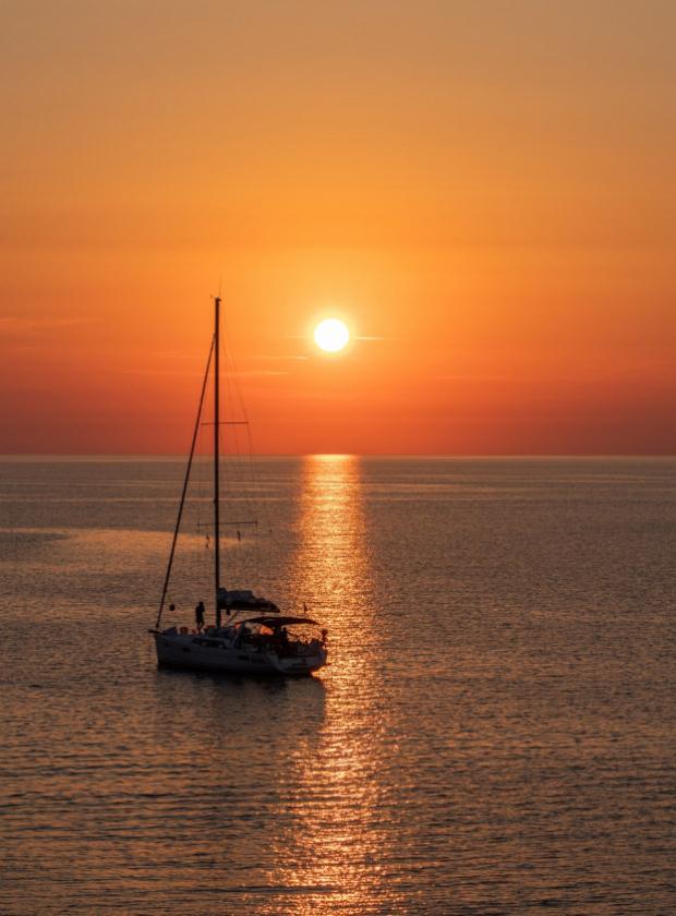 Barca a vela al tramonto, riflessi dorati sul mare calmo.